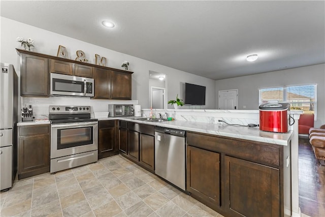 kitchen featuring kitchen peninsula, dark brown cabinets, stainless steel appliances, and sink