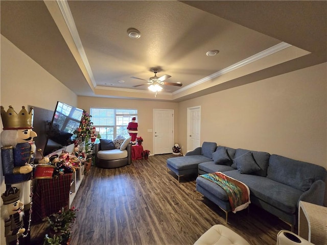 living room with dark hardwood / wood-style flooring, a tray ceiling, ceiling fan, and ornamental molding