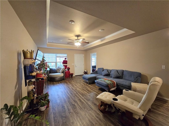 living room featuring ornamental molding, a tray ceiling, ceiling fan, and dark wood-type flooring