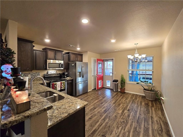 kitchen with appliances with stainless steel finishes, dark hardwood / wood-style flooring, light stone counters, sink, and a chandelier