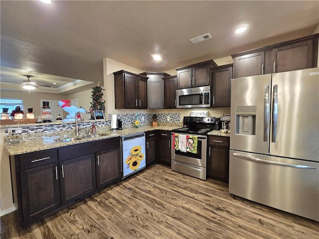 kitchen with sink, hardwood / wood-style flooring, light stone countertops, appliances with stainless steel finishes, and dark brown cabinets