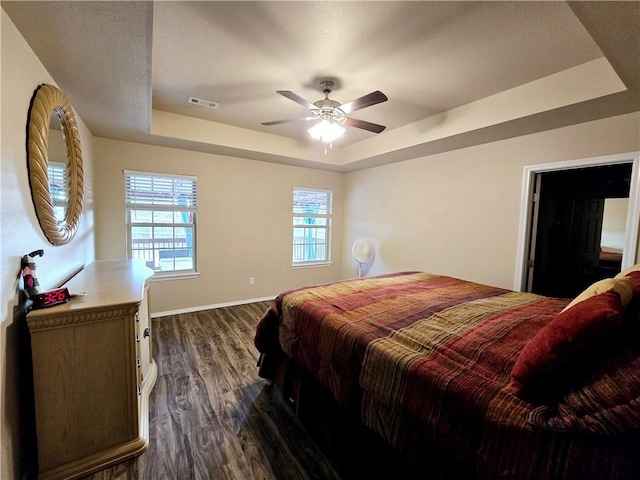 bedroom with dark hardwood / wood-style floors, ceiling fan, and a raised ceiling