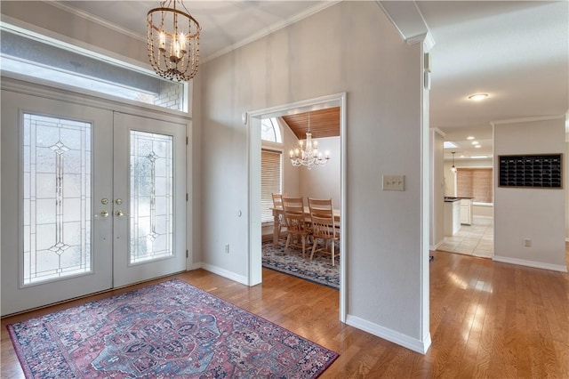 foyer entrance featuring a chandelier, french doors, light hardwood / wood-style floors, and crown molding