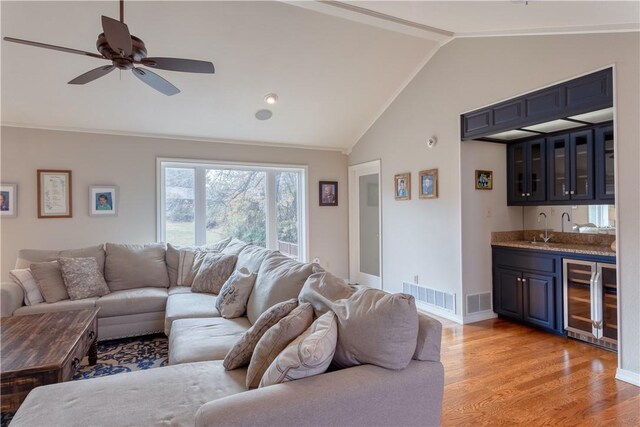 living room with ceiling fan, beverage cooler, wet bar, light hardwood / wood-style flooring, and lofted ceiling