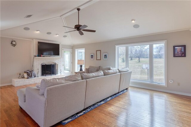 living room featuring ceiling fan, light hardwood / wood-style floors, lofted ceiling, and a brick fireplace