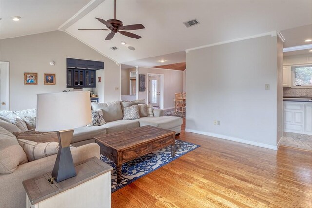 living room with ceiling fan, ornamental molding, lofted ceiling, and light wood-type flooring