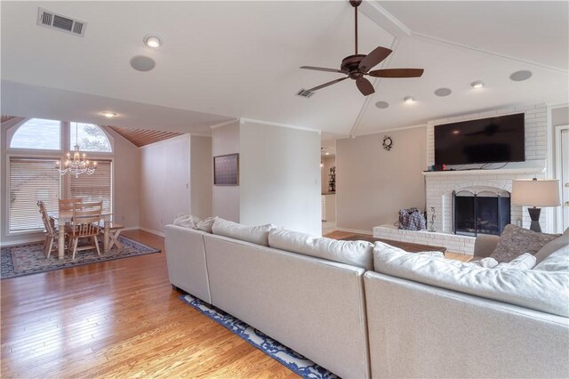 living room featuring a brick fireplace, ceiling fan with notable chandelier, vaulted ceiling, crown molding, and wood-type flooring