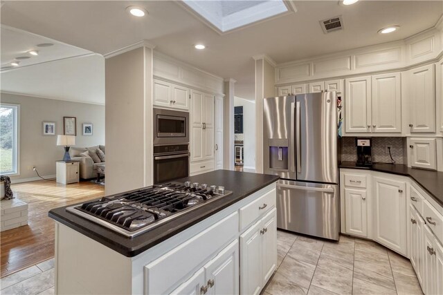 kitchen with backsplash, stainless steel appliances, white cabinetry, and a kitchen island