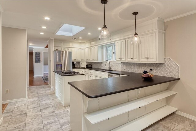 kitchen featuring kitchen peninsula, appliances with stainless steel finishes, a skylight, sink, and white cabinetry