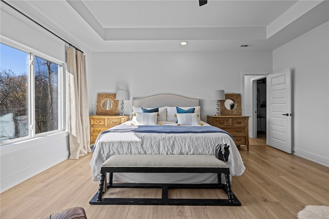 bedroom with light wood-type flooring and a tray ceiling