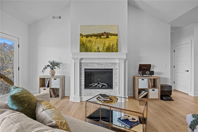 living room with a stone fireplace, wood-type flooring, and vaulted ceiling