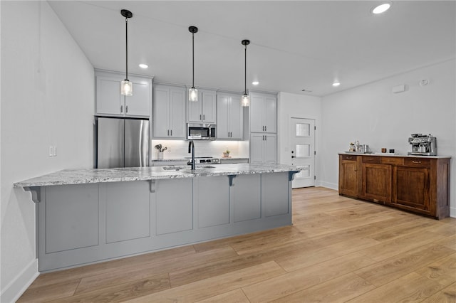 kitchen featuring light stone countertops, appliances with stainless steel finishes, decorative light fixtures, light hardwood / wood-style floors, and kitchen peninsula