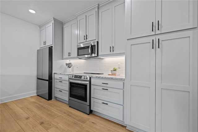 kitchen featuring decorative backsplash, light stone counters, light wood-type flooring, and appliances with stainless steel finishes