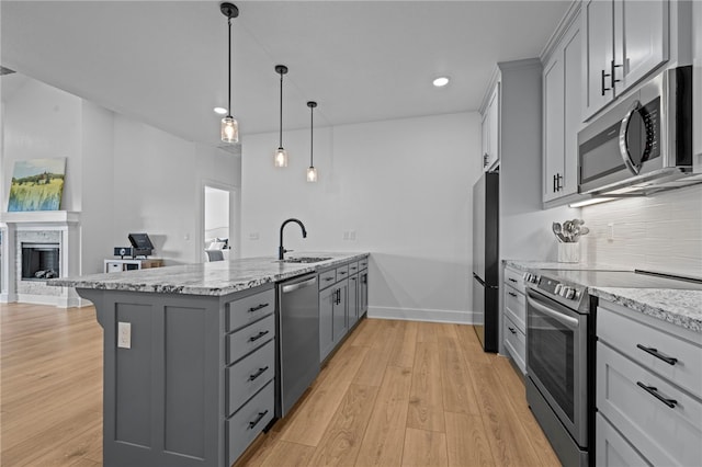 kitchen featuring sink, gray cabinets, light hardwood / wood-style floors, light stone counters, and stainless steel appliances