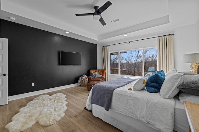 bedroom with ceiling fan, a tray ceiling, and light hardwood / wood-style flooring