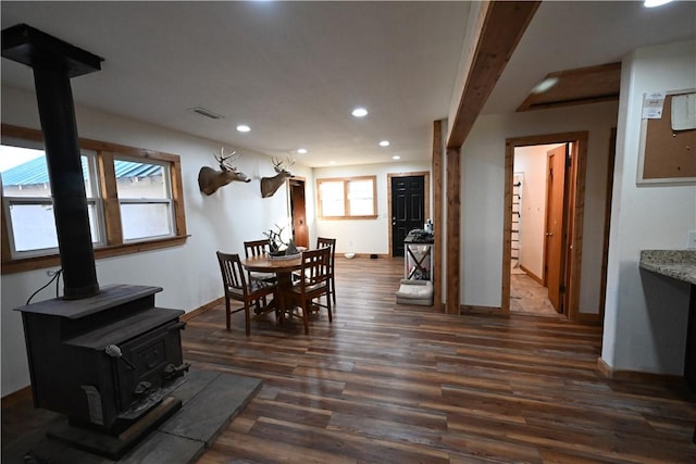 dining area with beamed ceiling, dark hardwood / wood-style flooring, and a wood stove