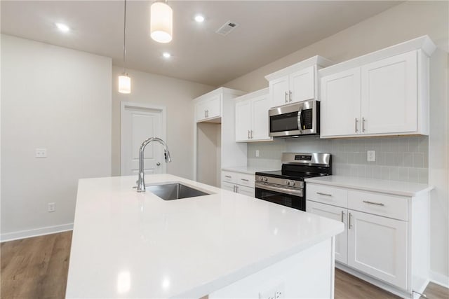 kitchen with appliances with stainless steel finishes, sink, a center island with sink, and pendant lighting