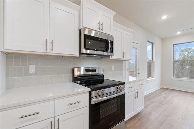 kitchen featuring backsplash, light hardwood / wood-style flooring, white cabinets, and appliances with stainless steel finishes