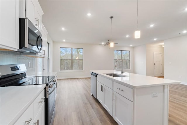 kitchen with sink, white cabinetry, decorative light fixtures, appliances with stainless steel finishes, and a kitchen island with sink