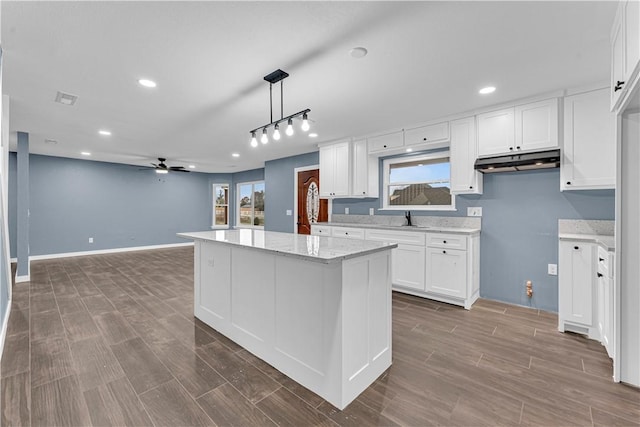 kitchen with ceiling fan, light stone countertops, a kitchen island, decorative light fixtures, and white cabinets