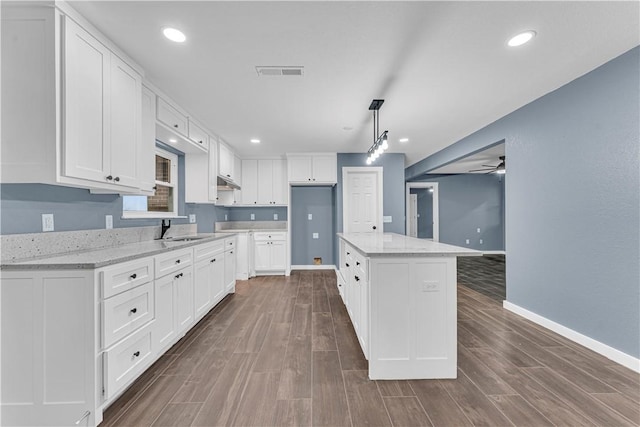 kitchen featuring light stone countertops, ceiling fan, decorative light fixtures, white cabinets, and a center island