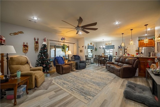 living room with ceiling fan with notable chandelier and light wood-type flooring