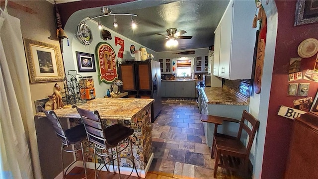 kitchen with white cabinetry, ceiling fan, light stone countertops, kitchen peninsula, and a kitchen bar