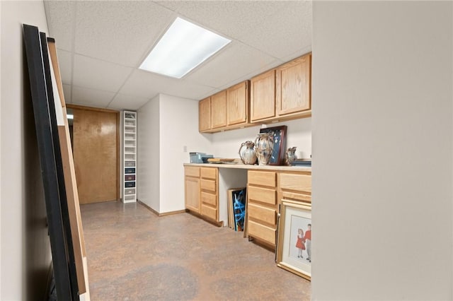 kitchen featuring a paneled ceiling, built in desk, light brown cabinetry, and concrete flooring