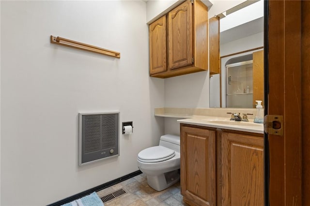 bathroom featuring heating unit, vanity, a shower with shower door, and toilet