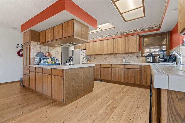 kitchen with sink, white refrigerator, backsplash, a textured ceiling, and light wood-type flooring