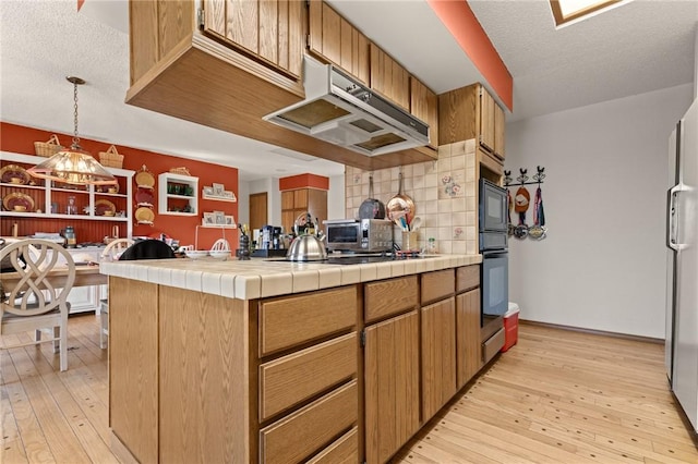 kitchen with decorative backsplash, a textured ceiling, light wood-type flooring, and tile countertops