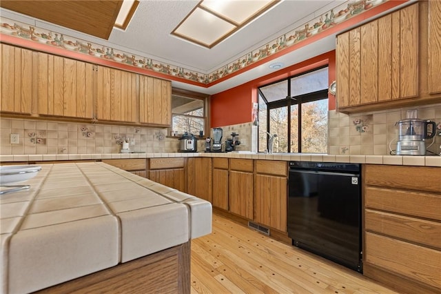 kitchen featuring decorative backsplash, sink, dishwasher, light hardwood / wood-style floors, and tile counters