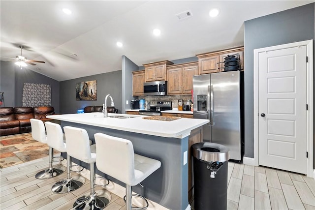 kitchen with a breakfast bar, a center island with sink, sink, ceiling fan, and stainless steel appliances