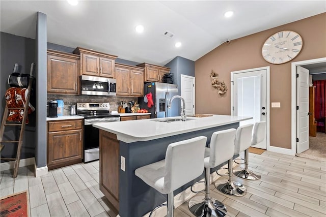 kitchen featuring decorative backsplash, appliances with stainless steel finishes, vaulted ceiling, sink, and an island with sink