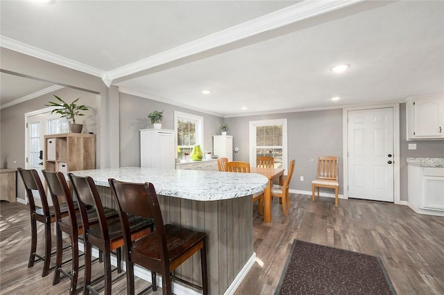 kitchen with dark hardwood / wood-style floors, a kitchen bar, white cabinetry, and crown molding