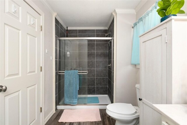 bathroom featuring hardwood / wood-style flooring, toilet, ornamental molding, and a shower with door