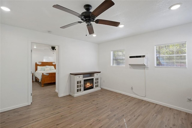 unfurnished living room with a wall unit AC, a textured ceiling, a wealth of natural light, and light hardwood / wood-style flooring