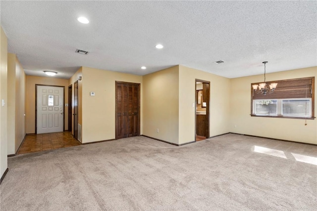 empty room with light carpet, a textured ceiling, and a chandelier