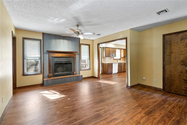 unfurnished living room with a tile fireplace, ceiling fan, dark wood-type flooring, and a textured ceiling