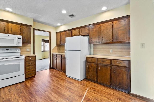 kitchen featuring a textured ceiling, tasteful backsplash, hardwood / wood-style floors, and white appliances