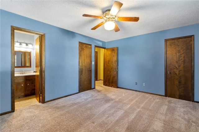 unfurnished bedroom with two closets, ensuite bathroom, ceiling fan, a textured ceiling, and light colored carpet