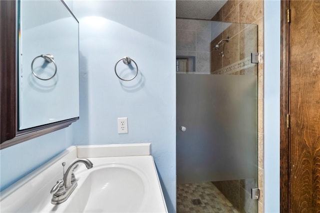 bathroom featuring a textured ceiling, a shower with shower door, and sink