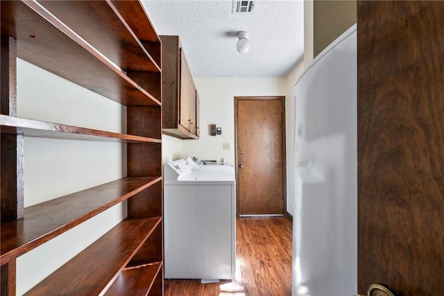 clothes washing area with cabinets, a textured ceiling, dark hardwood / wood-style flooring, and washer and dryer