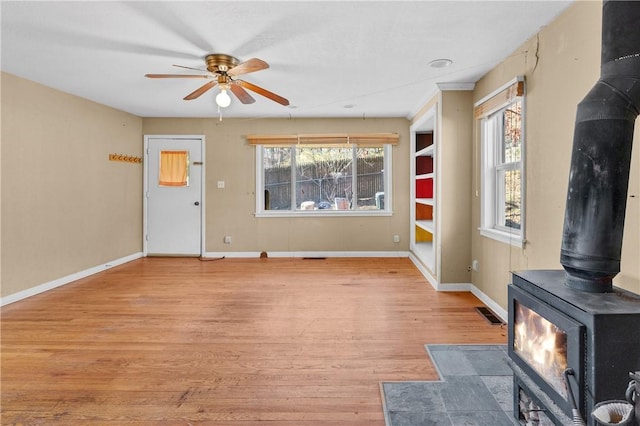 unfurnished living room featuring light hardwood / wood-style floors, a wood stove, and ceiling fan