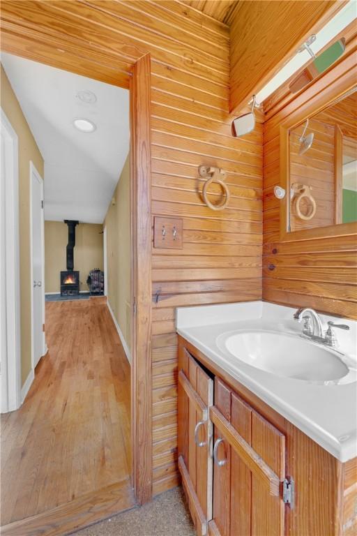 bathroom featuring vanity, wood walls, wood-type flooring, and a wood stove