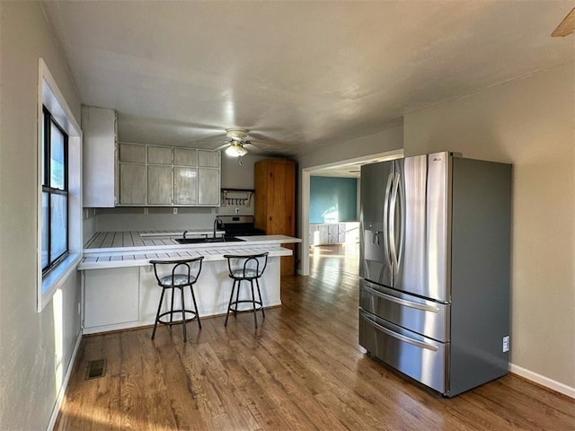 kitchen featuring a breakfast bar area, white cabinetry, tile countertops, kitchen peninsula, and stainless steel appliances