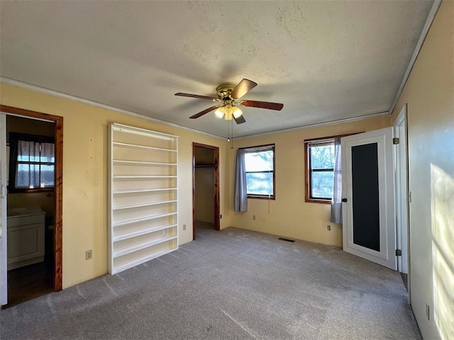 unfurnished bedroom with ensuite bathroom, a textured ceiling, ornamental molding, carpet flooring, and ceiling fan