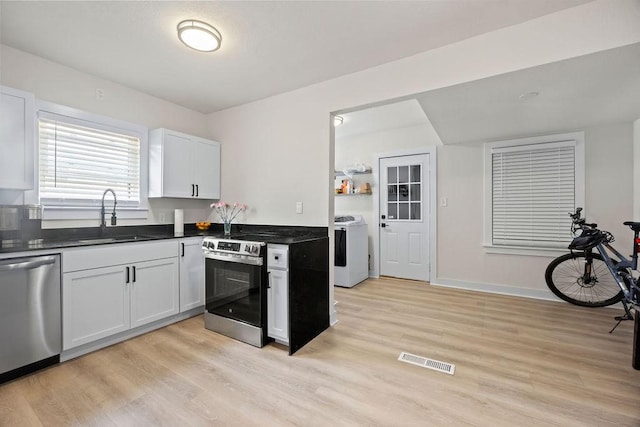 kitchen featuring white cabinetry, sink, stainless steel appliances, washing machine and dryer, and light hardwood / wood-style floors