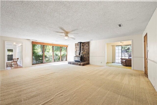 unfurnished living room with a healthy amount of sunlight, a textured ceiling, light carpet, and a wood stove