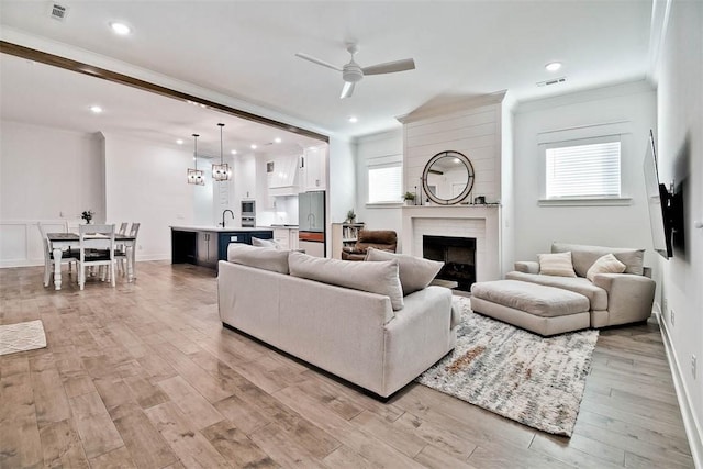 living room featuring light wood-type flooring, ceiling fan, crown molding, and sink